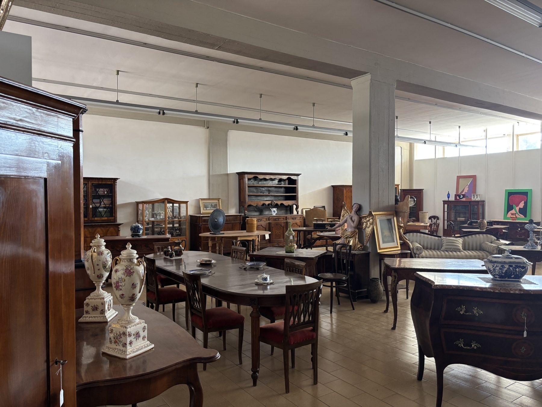 Sala da pranzo dello showroom Angelini allestita con anfore in porcellana e tavoli d'epoca